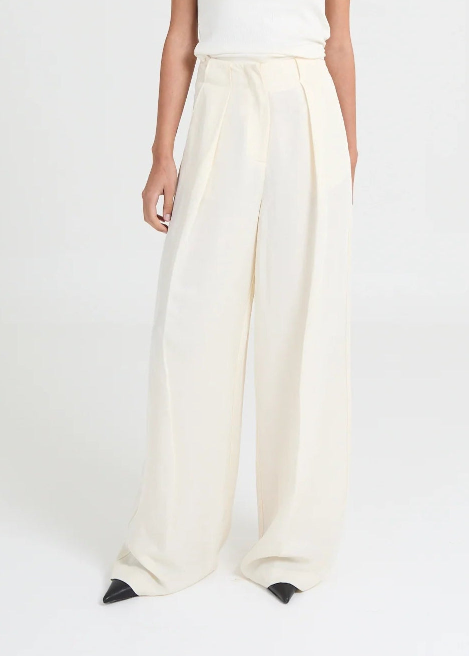 Tailored wide-leg trousers that are crafted from a slightly structured linen-blend fabric. Designed with an invisible high waistband and deep front pleats, they create a fluid yet defined silhouette. The elongated leg falls effortlessly to the floor, creating a refined essential that transitions seamlessly from modern daywear to elevated evening looks.