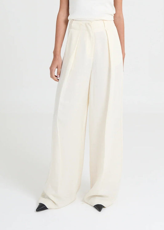 Tailored wide-leg trousers that are crafted from a slightly structured linen-blend fabric. Designed with an invisible high waistband and deep front pleats, they create a fluid yet defined silhouette. The elongated leg falls effortlessly to the floor, creating a refined essential that transitions seamlessly from modern daywear to elevated evening looks.